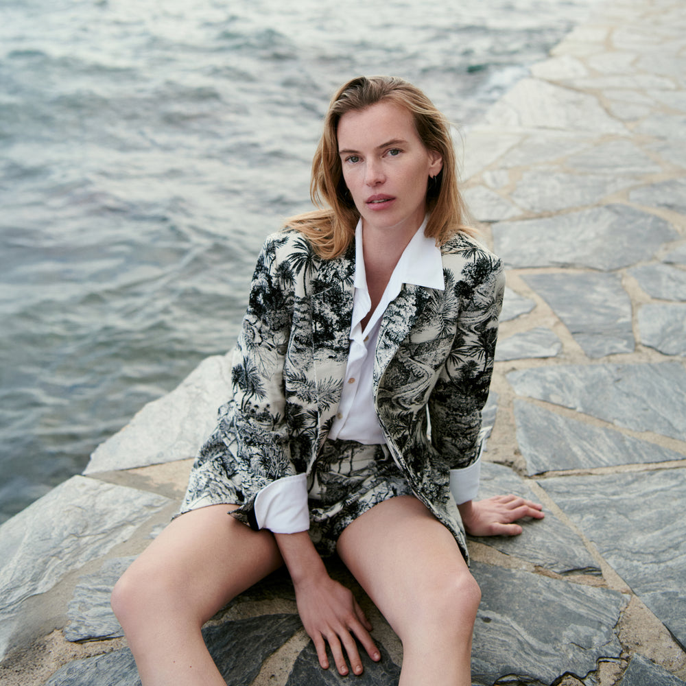 Woman sitting on a stone path by a body of water wearing a patterned outfit.