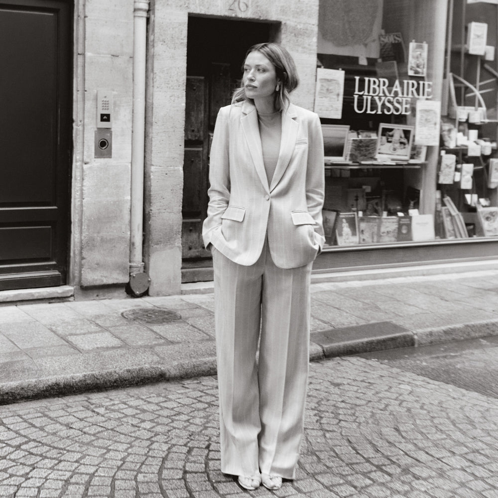 Woman in a light-colored suit standing on a street in front of a bookshop.