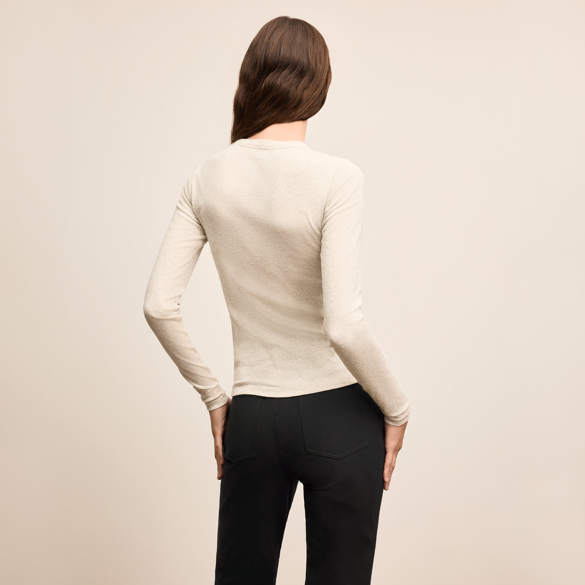 Person wearing a beige long-sleeve top and black pants on a beige background
