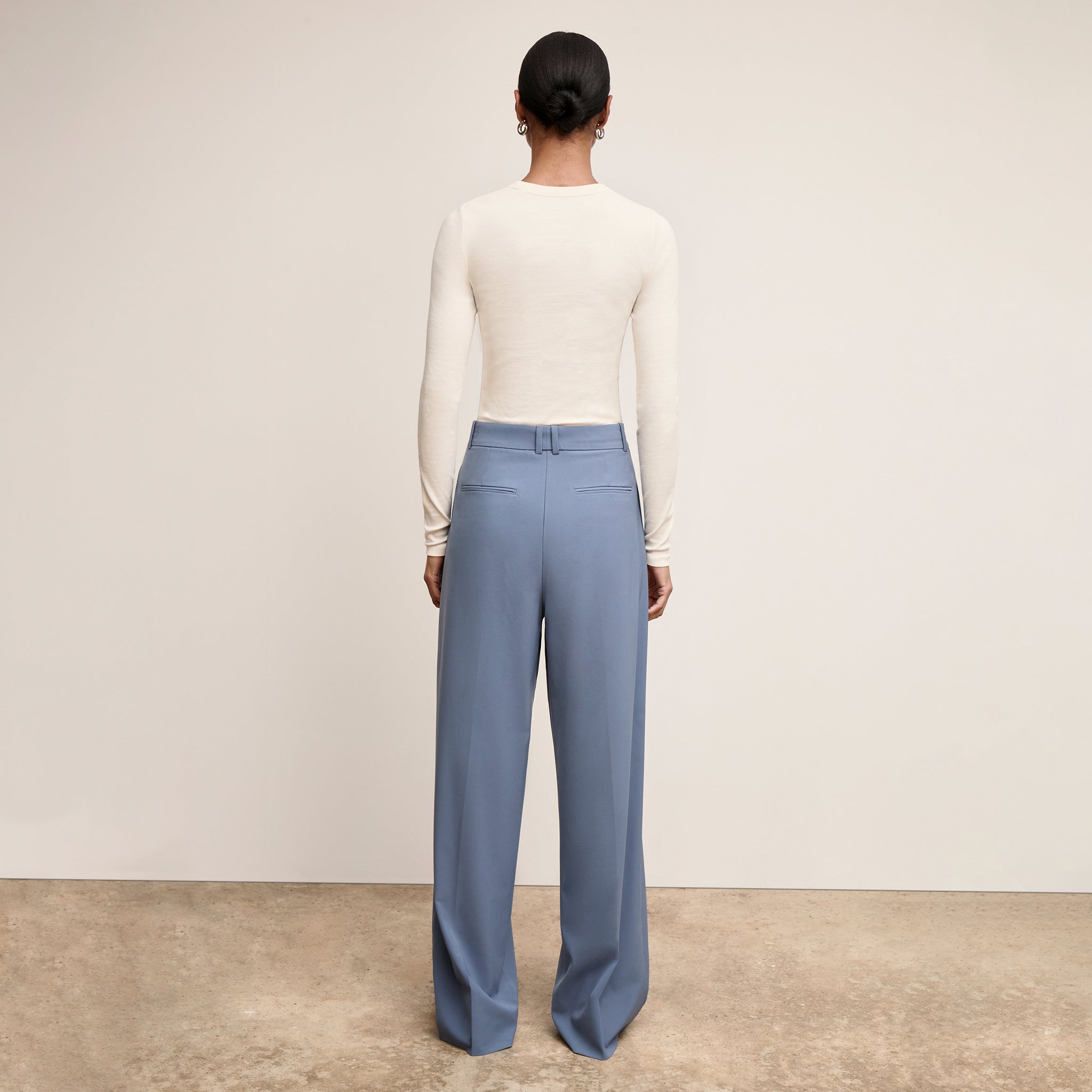 Woman wearing a white long-sleeve top and blue pants against a plain background