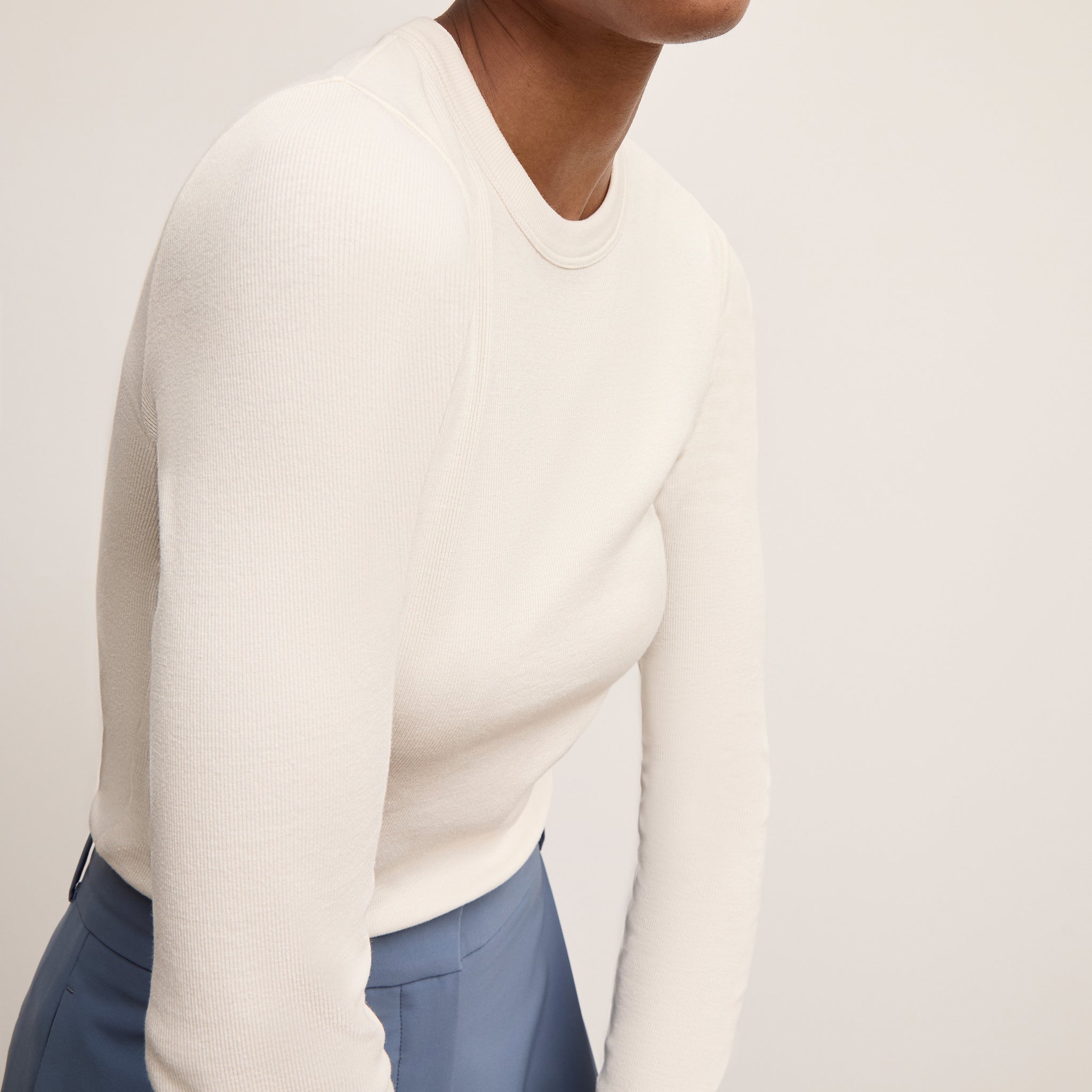 Person wearing a white sweater and blue pants on a plain background