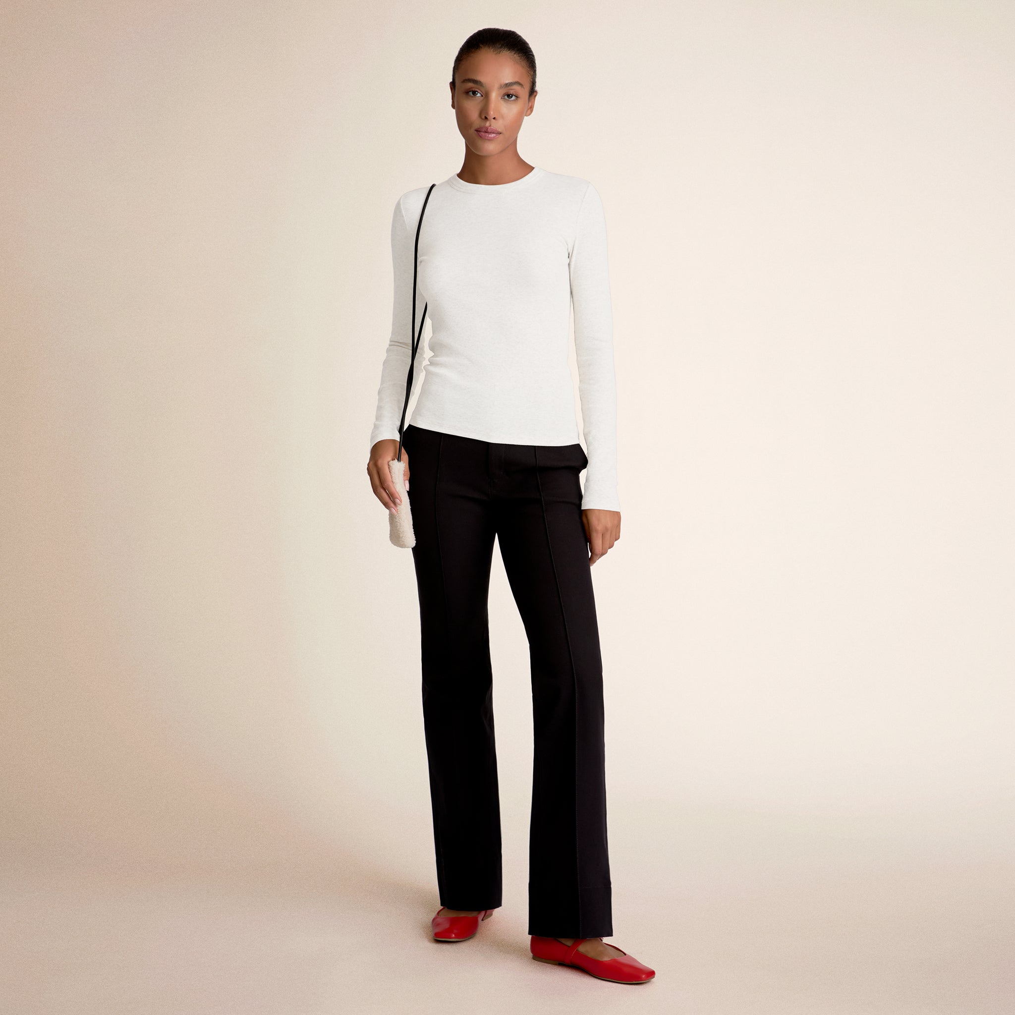 Woman wearing a white long-sleeve top, black pants, and red shoes on a beige background 