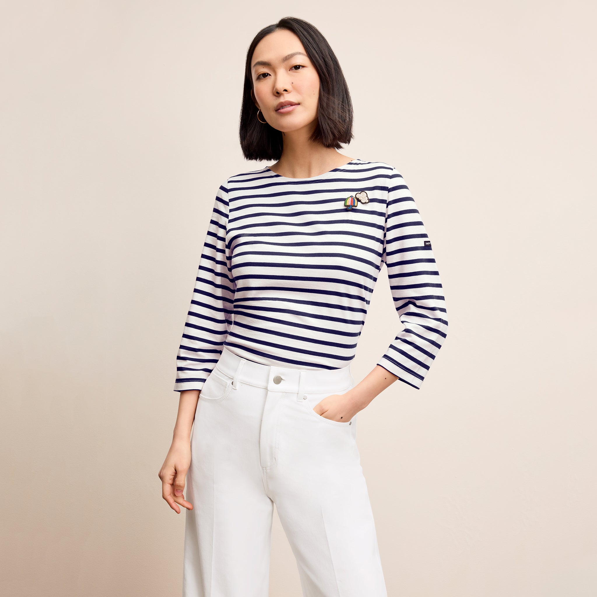 Woman wearing a striped shirt and white pants against a beige background 