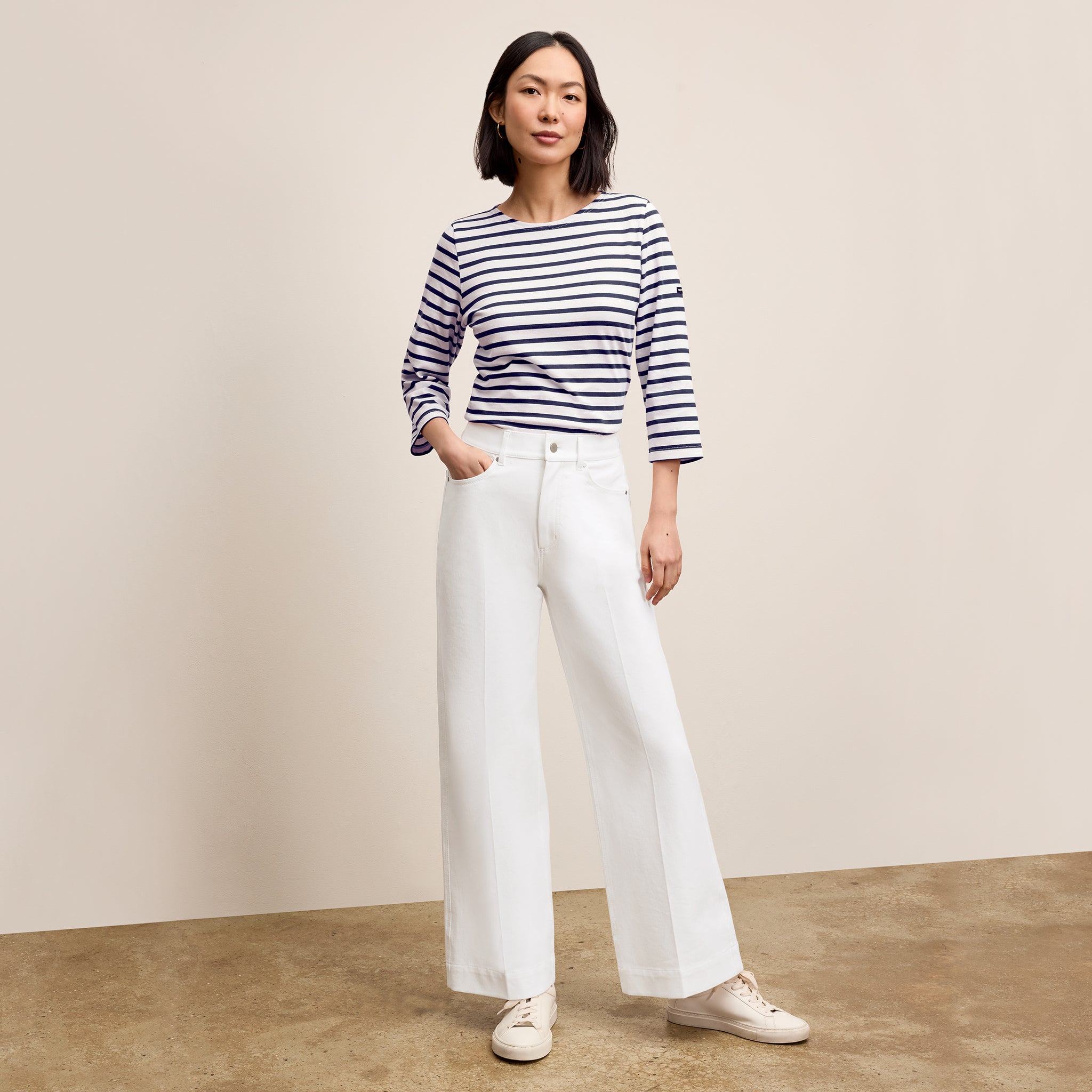 Woman wearing a striped shirt and white pants against a beige background