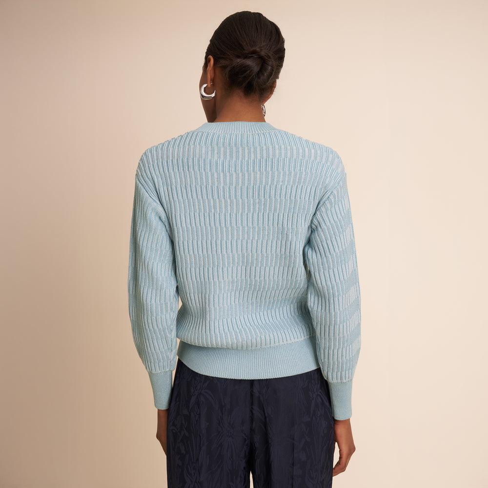 Person wearing a light blue sweater and dark pants on a beige background
