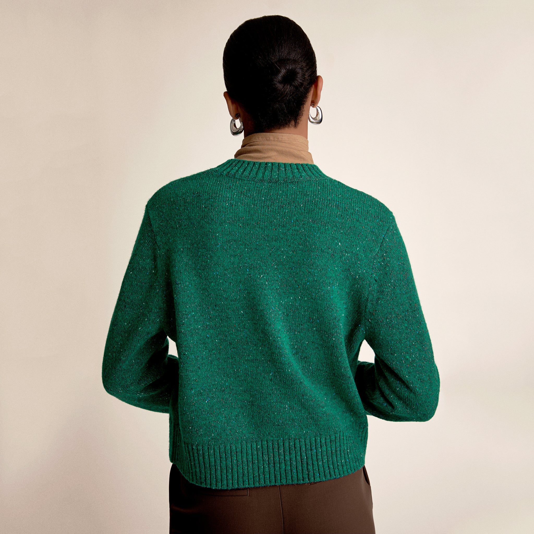 Person wearing a green sweater from behind on a beige background