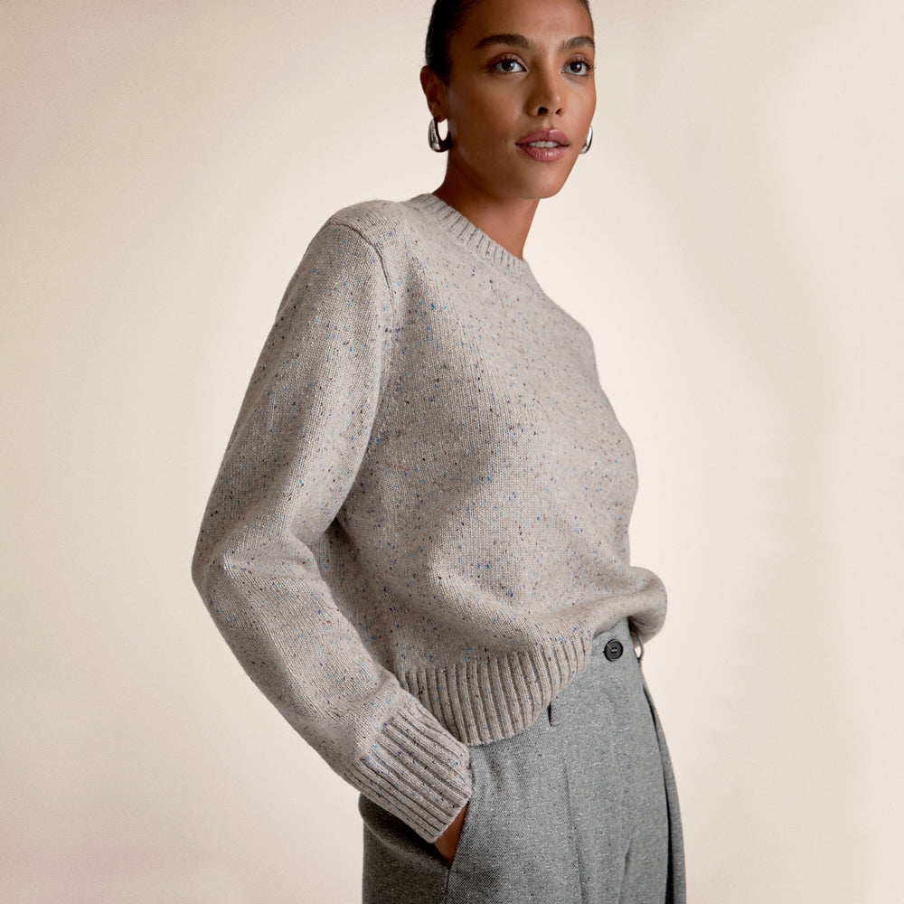 Woman wearing a gray sweater and pants against a beige background