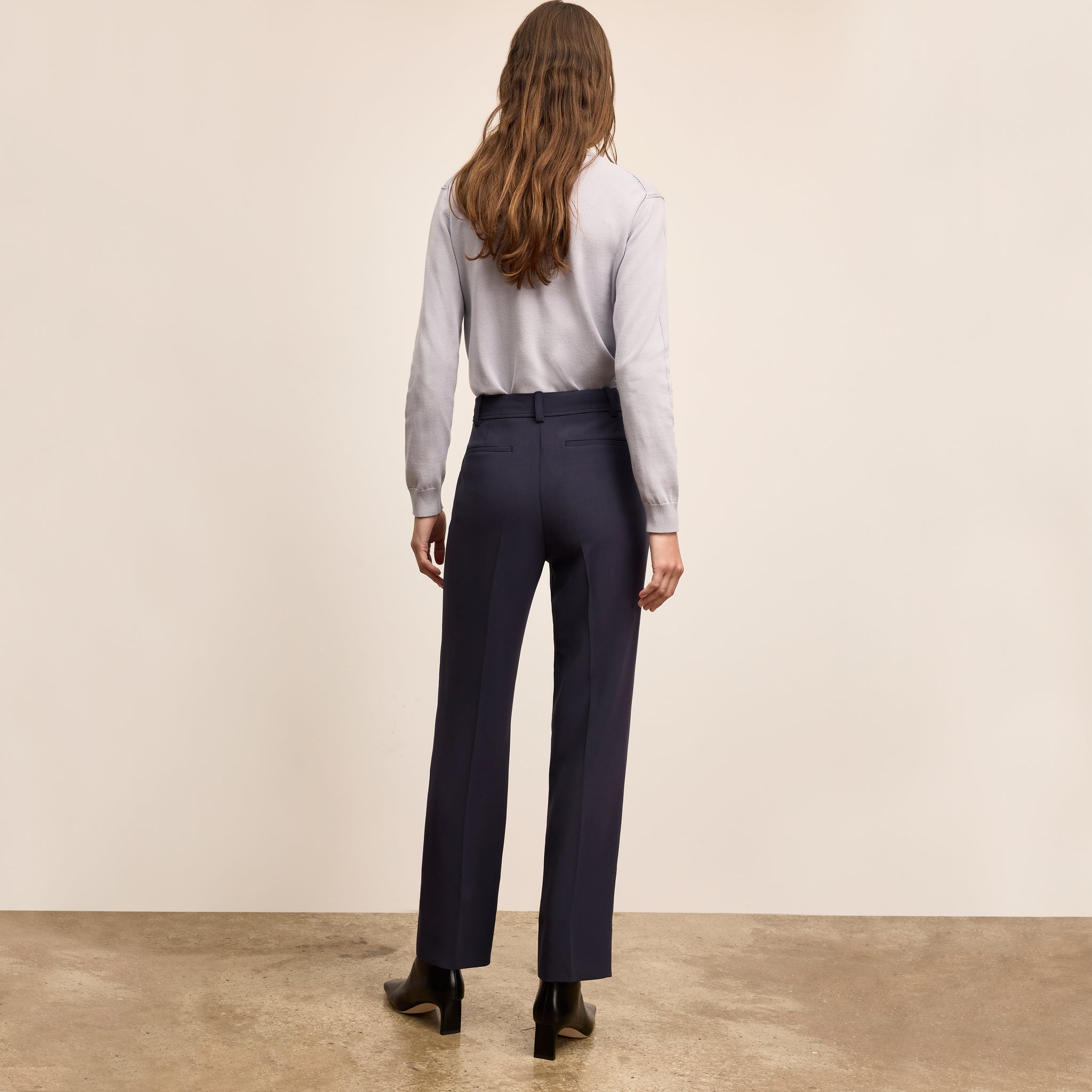 Person wearing a light gray shirt and dark blue pants against a beige background