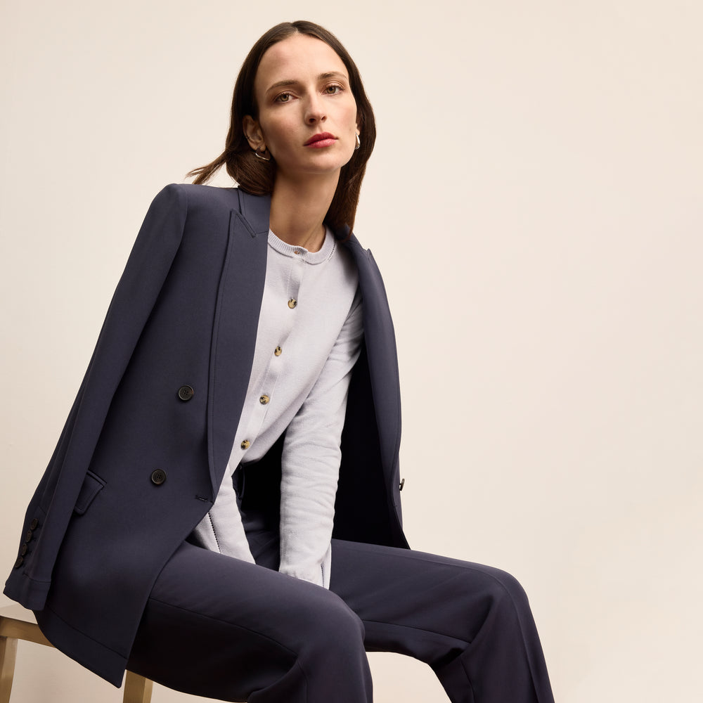 Woman wearing a navy suit sitting on a chair against a beige background