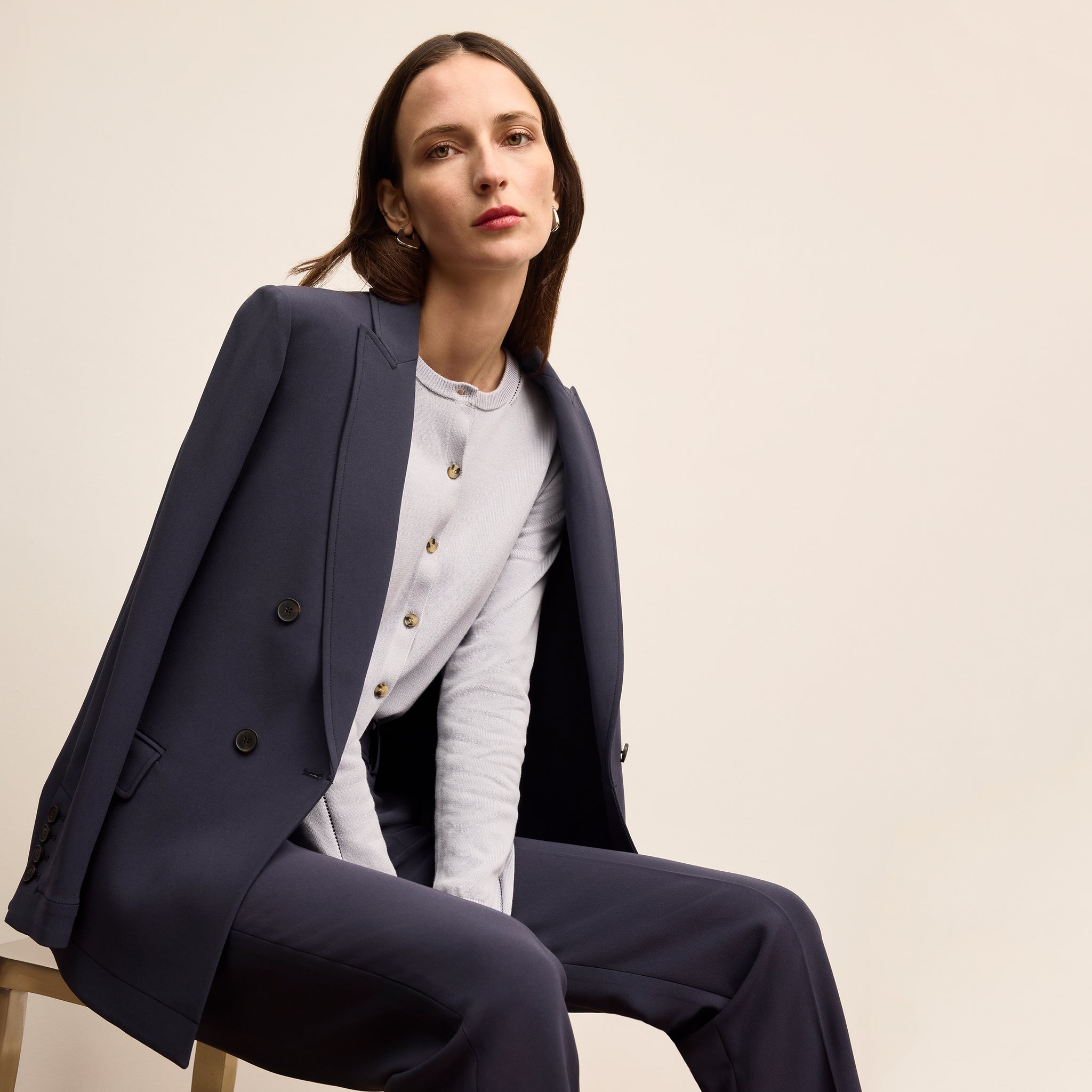 Woman wearing a navy suit sitting on a chair against a beige background 