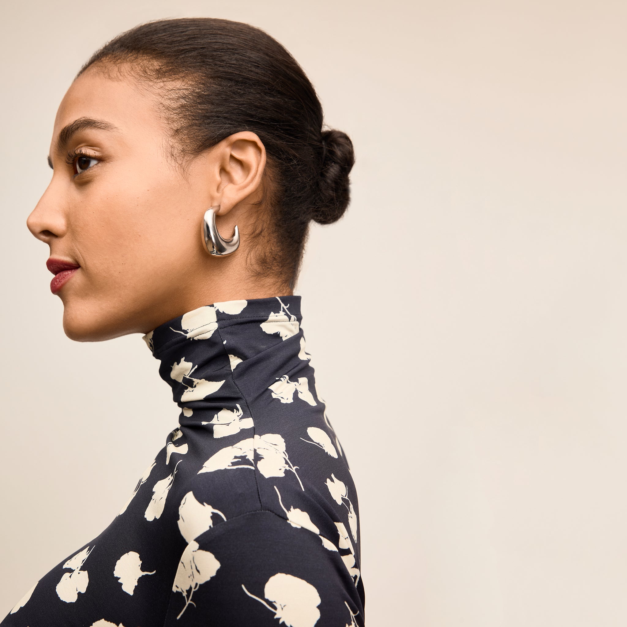 Woman wearing a navy blue top with white floral pattern against a beige background 