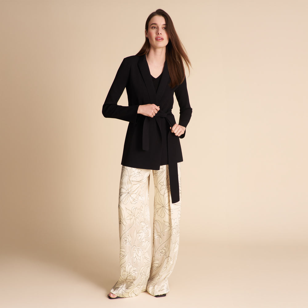 Woman wearing a black coat and gold patterned pants on a beige background