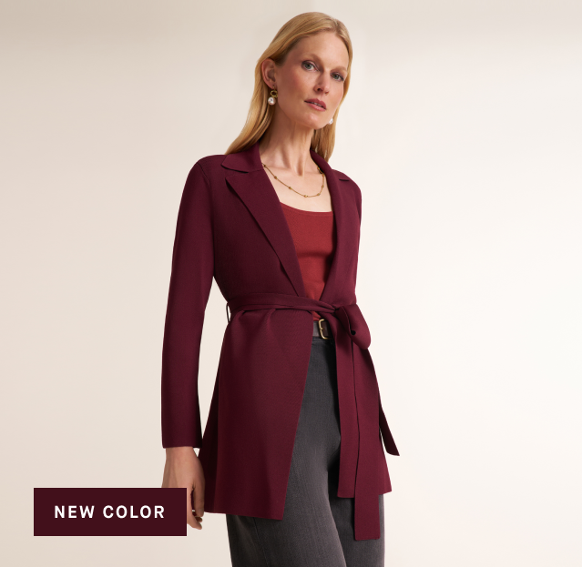 A woman models a long-sleeve wrap-style blazer in deep burgundy, worn over a matching burgundy top and gray trousers. The image has a warm beige studio background and a dark burgundy text box in the bottom-left corner that reads 'NEW COLOR'.