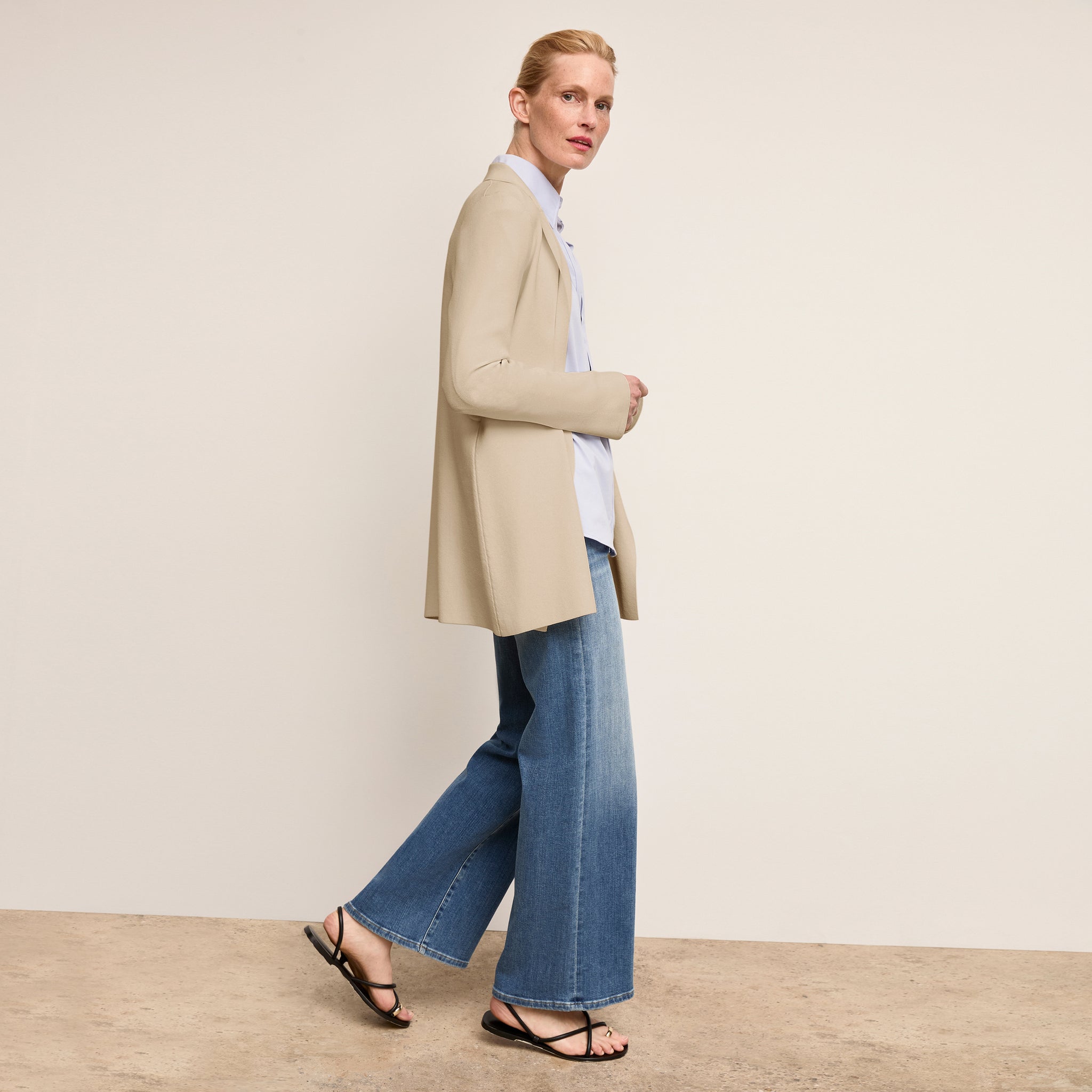 Woman wearing a beige coat and blue jeans against a plain background