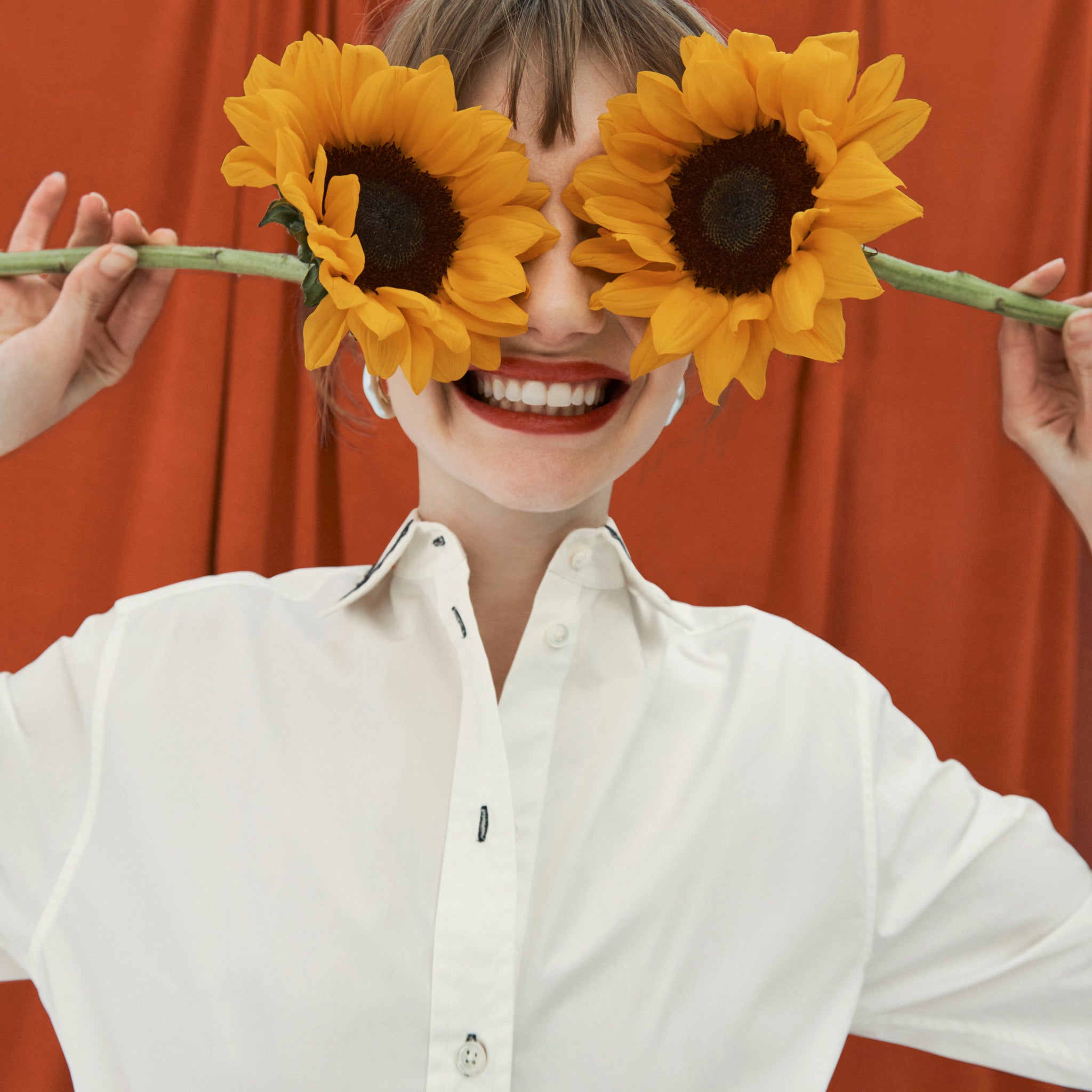 image of a woman holding sunflowers in front of her eyes wearing the mila top in embroidered poplin