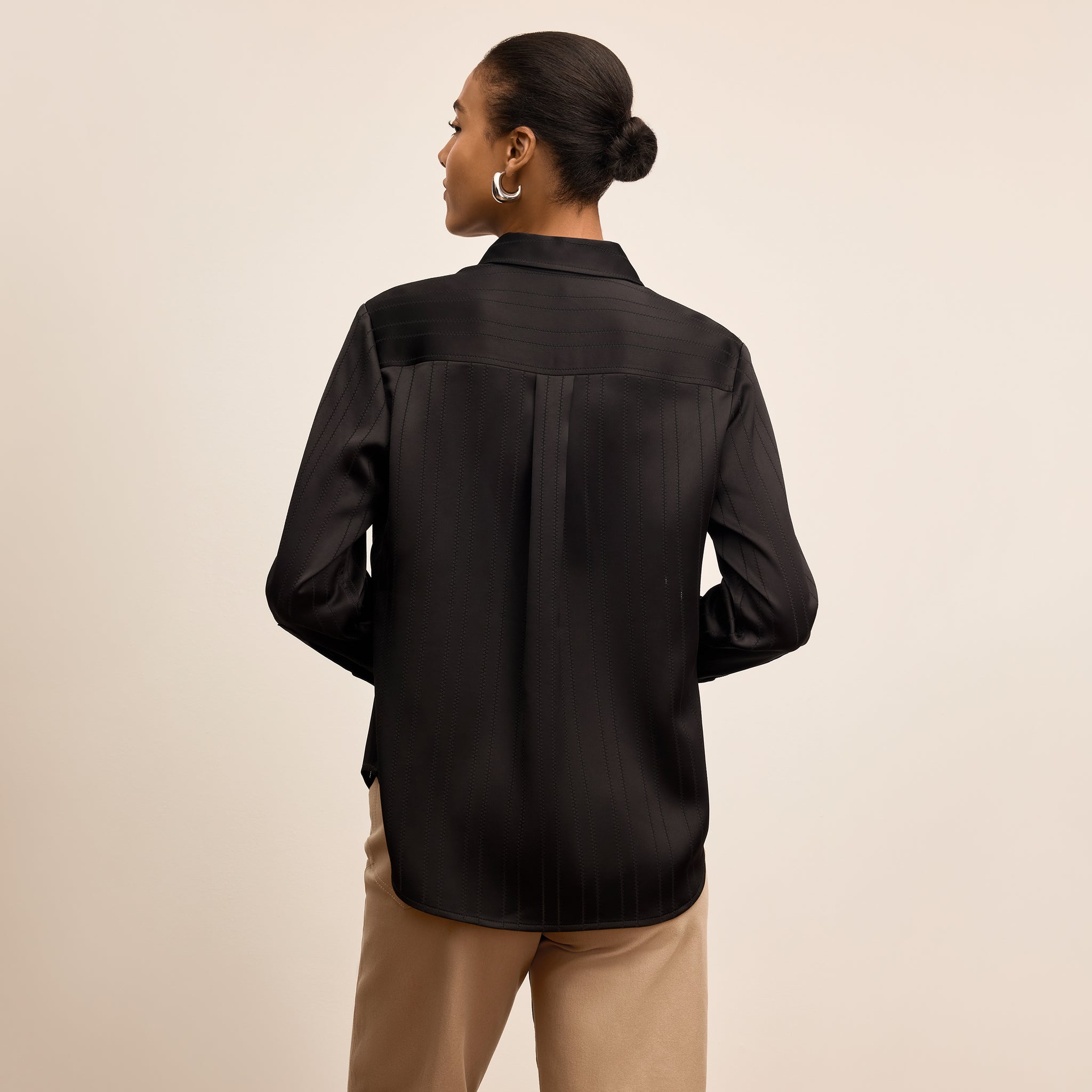 Person wearing a black satin shirt with a beige background
