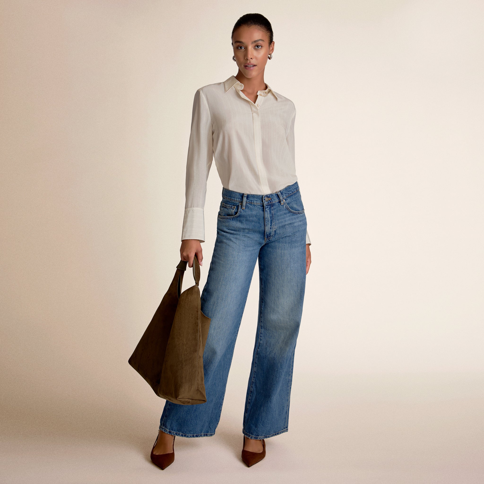 Woman wearing a white blouse and blue jeans, holding a brown bag on a beige background