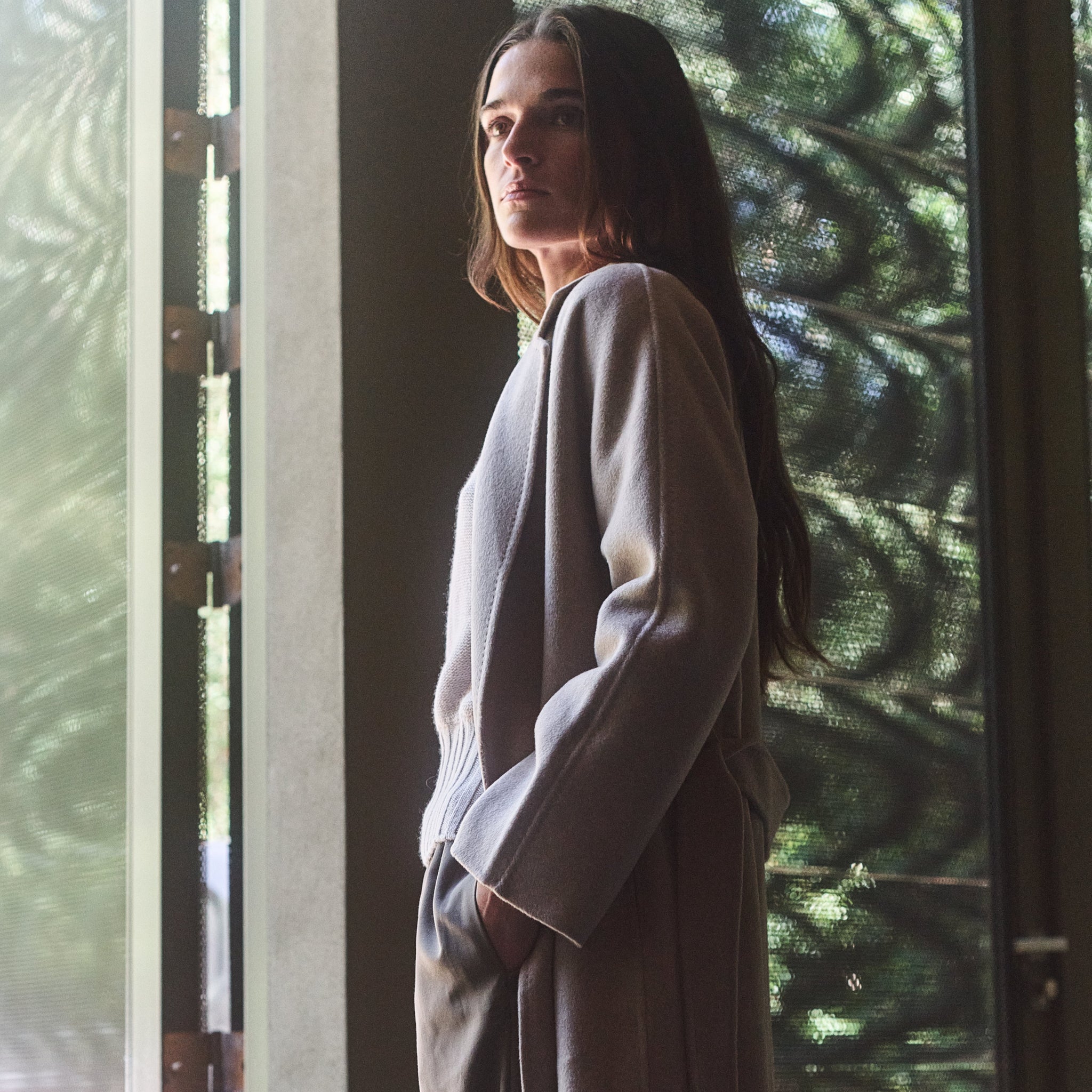 Person wearing a long coat standing in front of a glass door with a blurred outdoor background