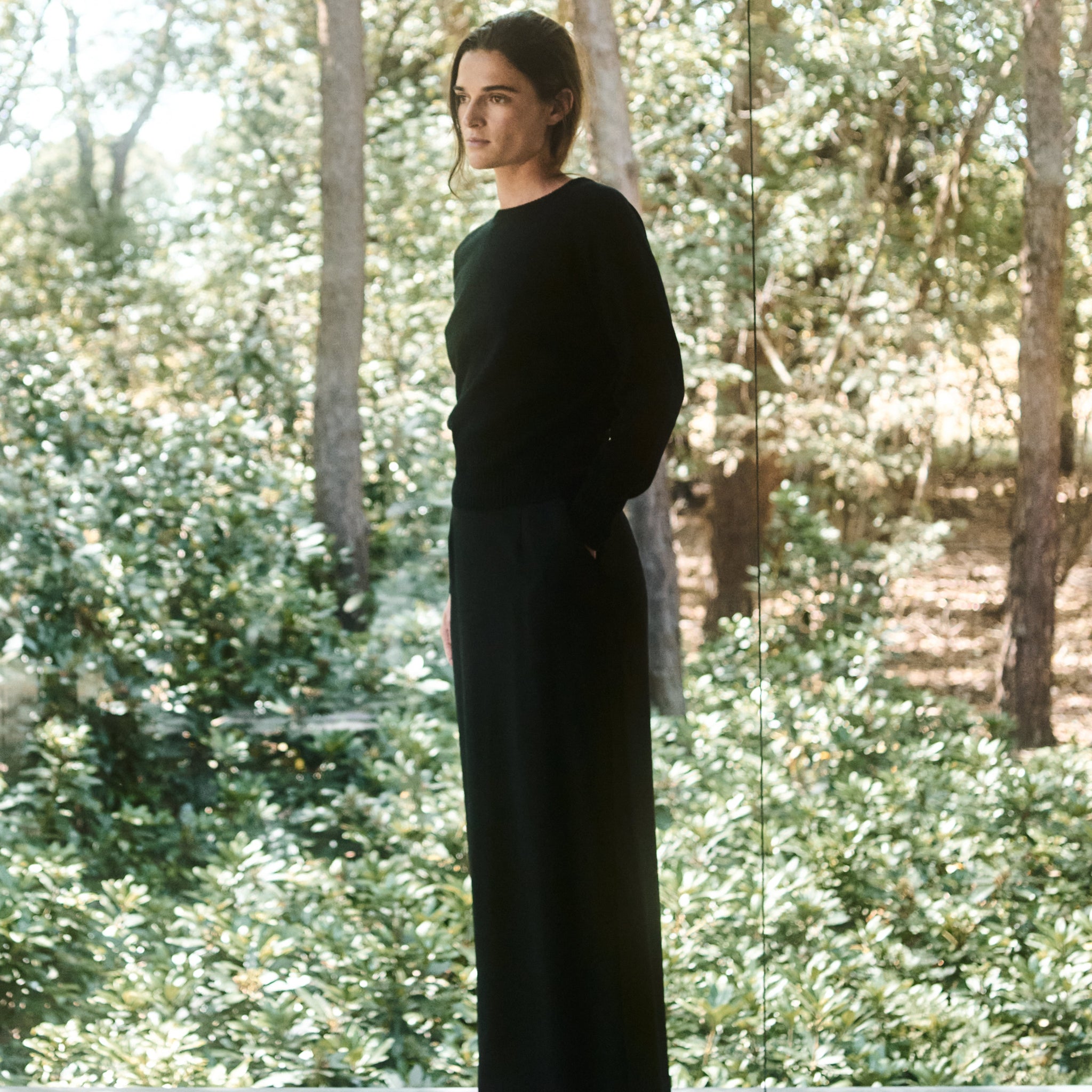 Person wearing a black outfit standing in a forested area