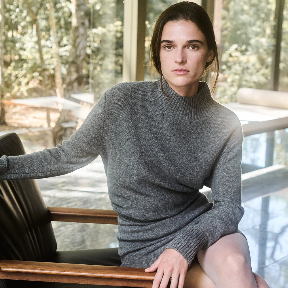 Woman in a gray sweater sitting on a wooden chair indoors with a blurred natural background