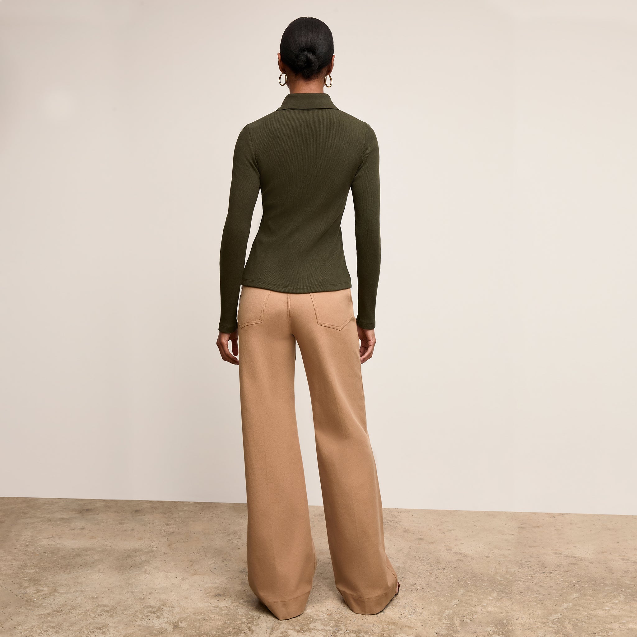 Woman wearing a green long-sleeve top and beige wide-leg pants on a plain background