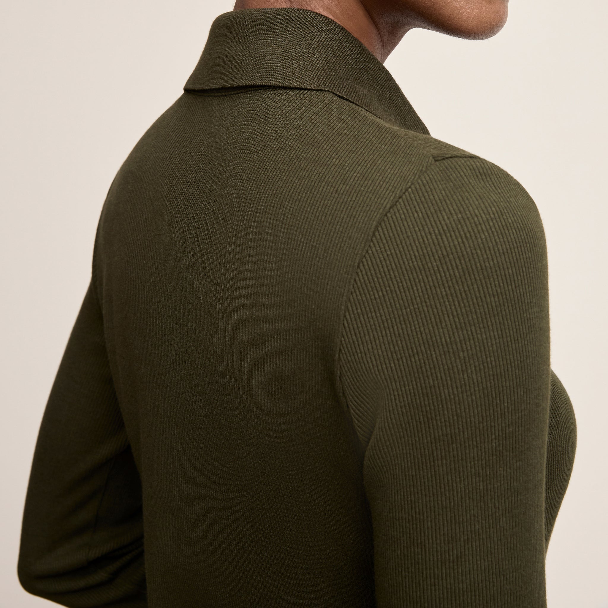 Person wearing a green ribbed sweater against a beige background