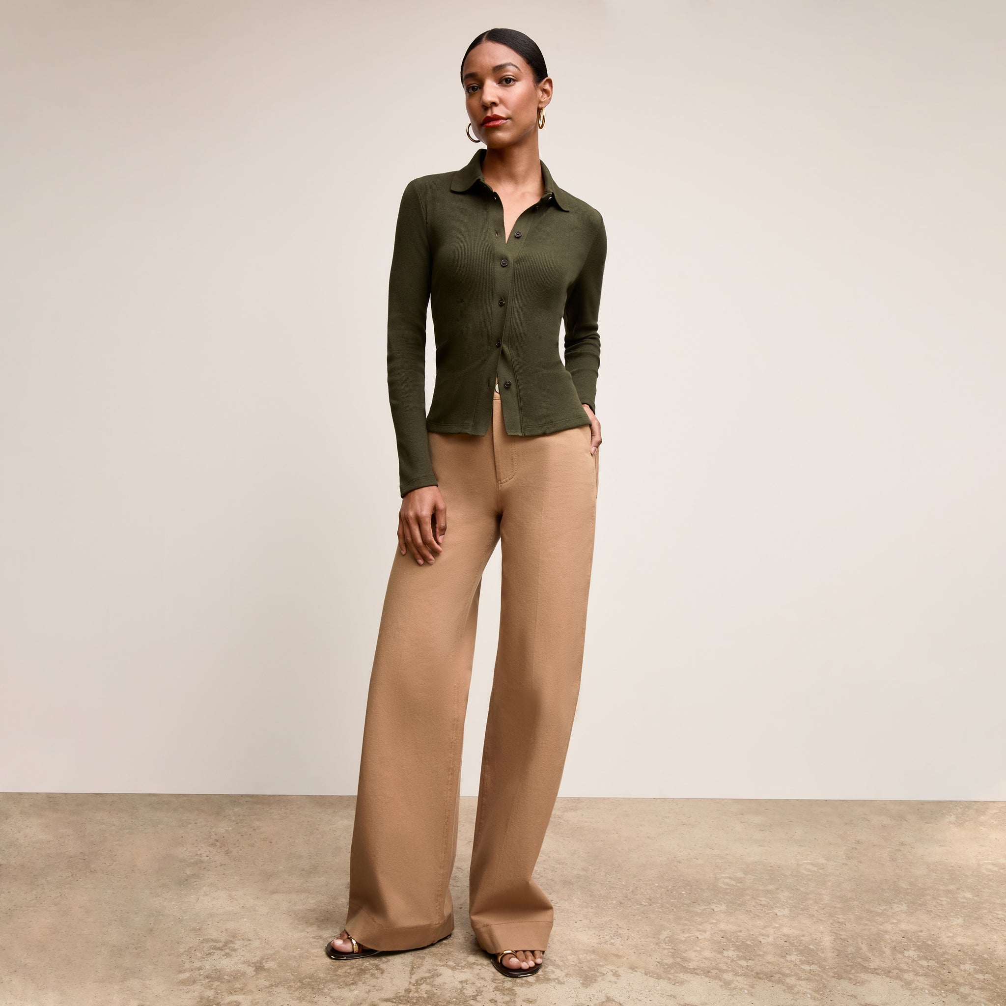 Woman wearing a green cardigan and beige pants against a neutral background 