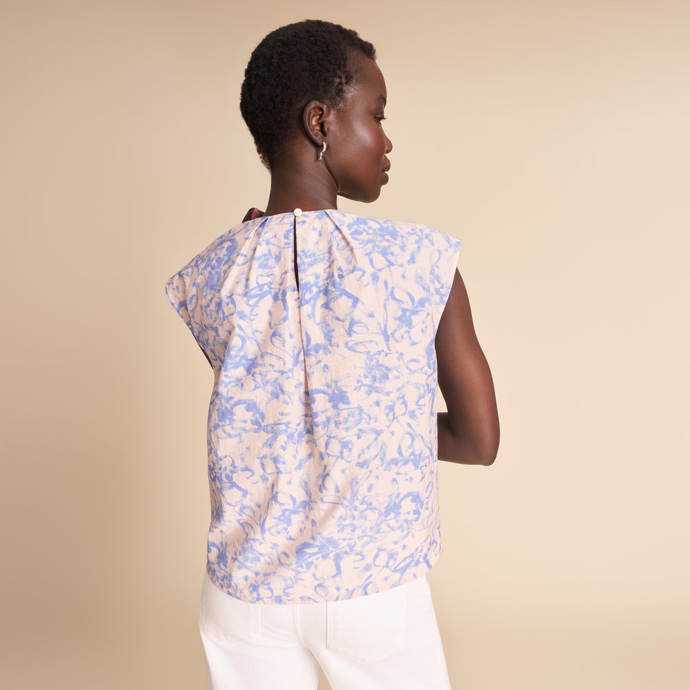 Woman wearing a floral blouse and white pants against a beige background