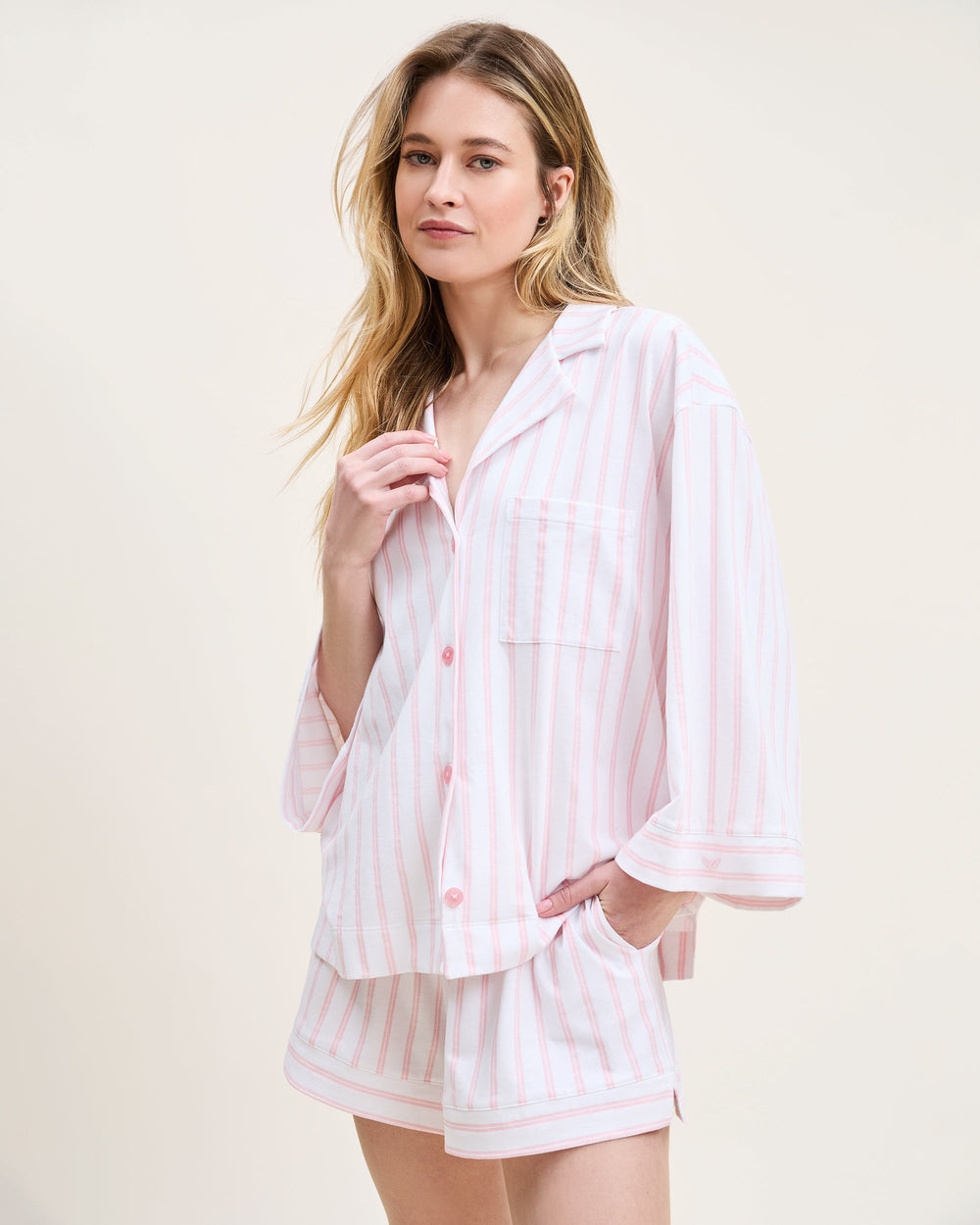 Woman wearing a light pink and white striped pajama set on a plain background