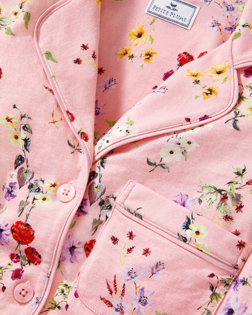 Close-up of a pink floral-patterned garment with 'Petite Plume' branding.
