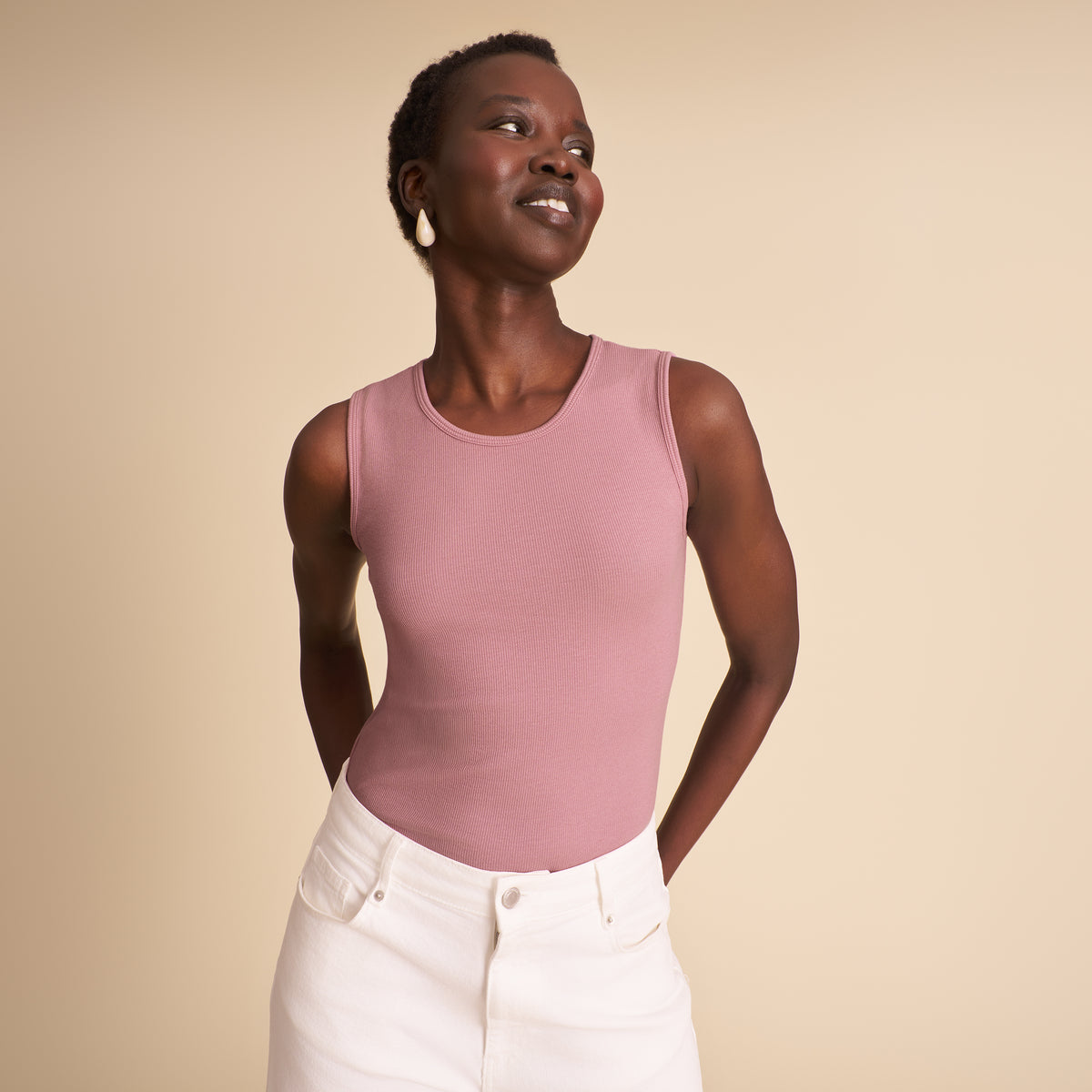 Woman wearing a pink sleeveless top and white pants against a beige background