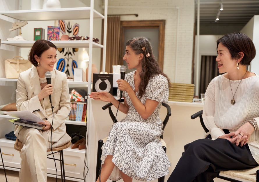 Three women in a room with one holding a microphone, another sitting in a wheelchair, and the third standing.