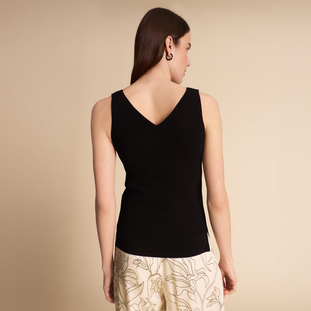 Woman wearing a black sleeveless top and beige pants against a plain background