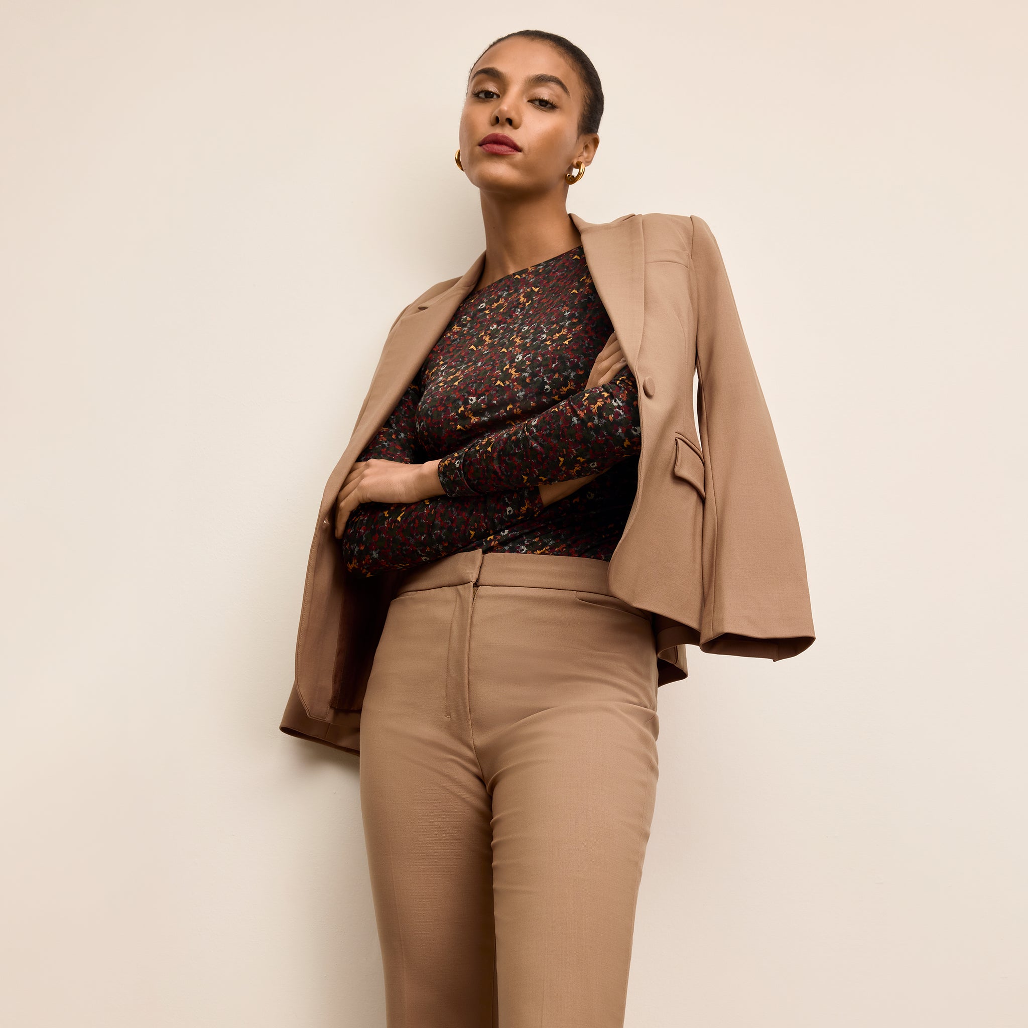 Woman wearing a beige blazer over a patterned top and beige pants on a plain background
