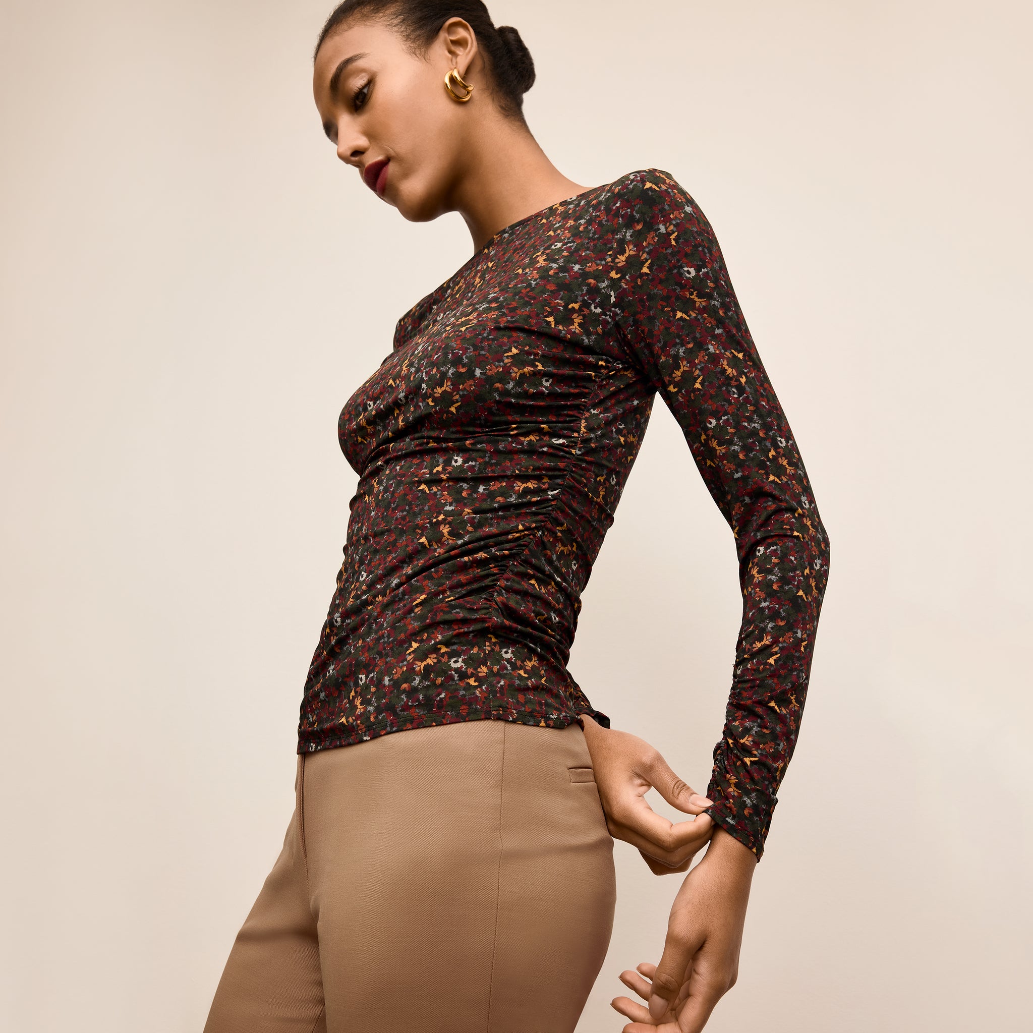 Woman wearing a patterned long-sleeve top and beige pants on a beige background 