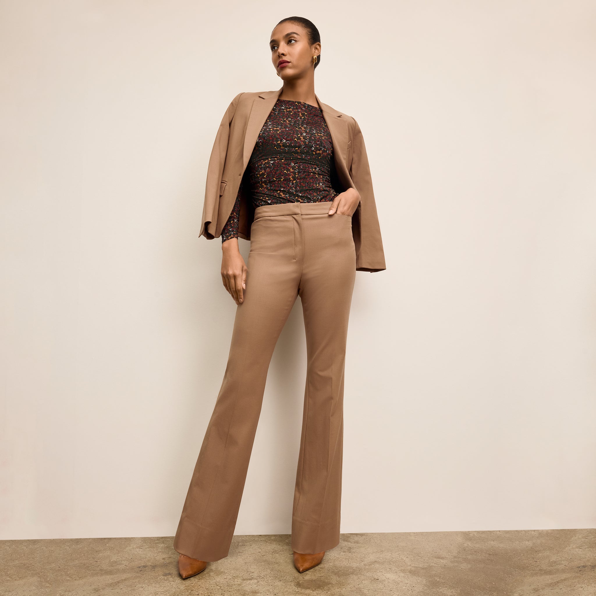 Woman wearing a beige blazer and pants with a patterned top against a plain background
