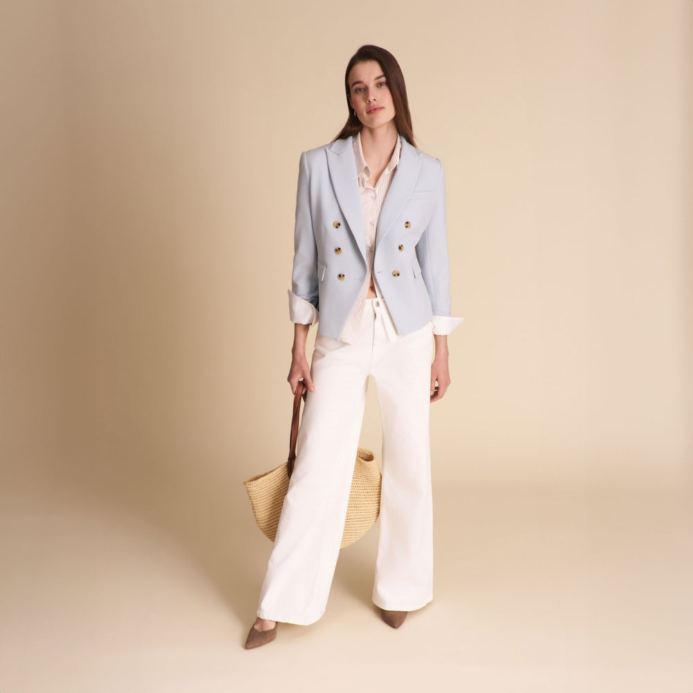 Woman wearing a light blue blazer and white pants on a beige background