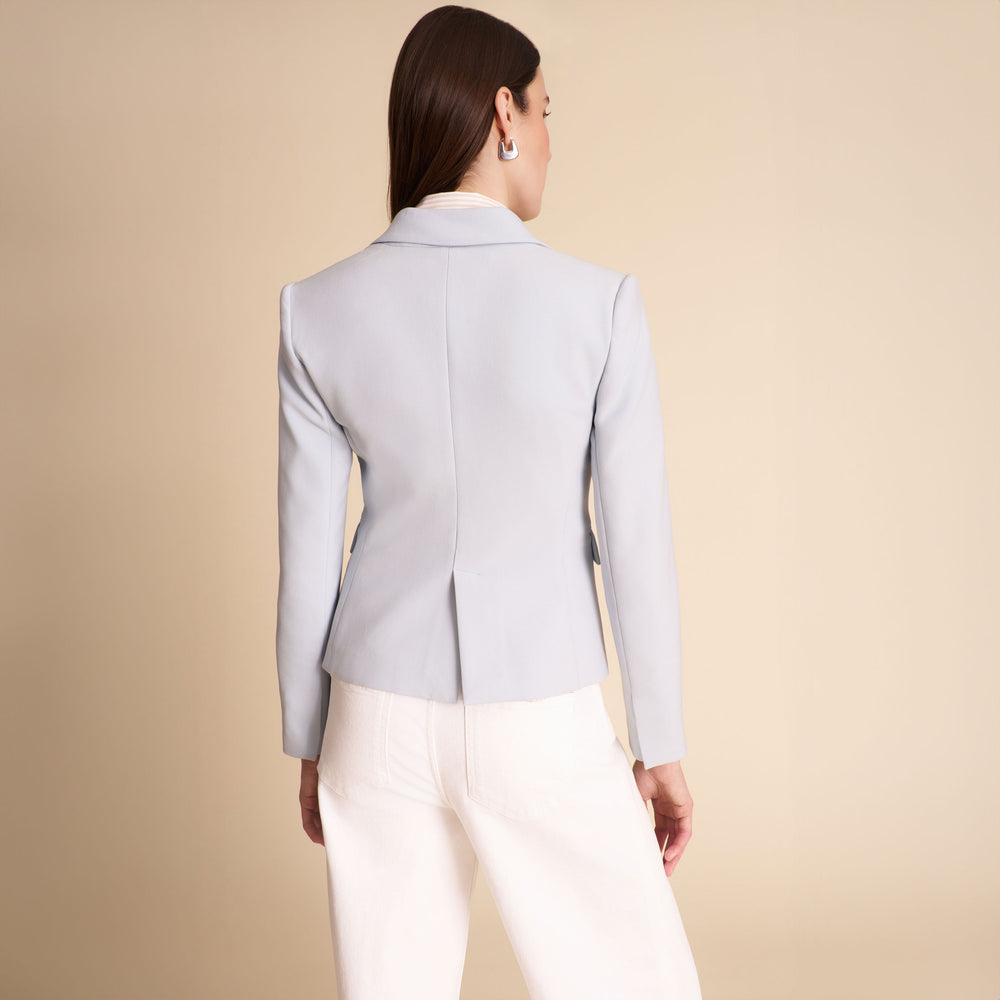 Woman wearing a light blue blazer and white pants on a beige background