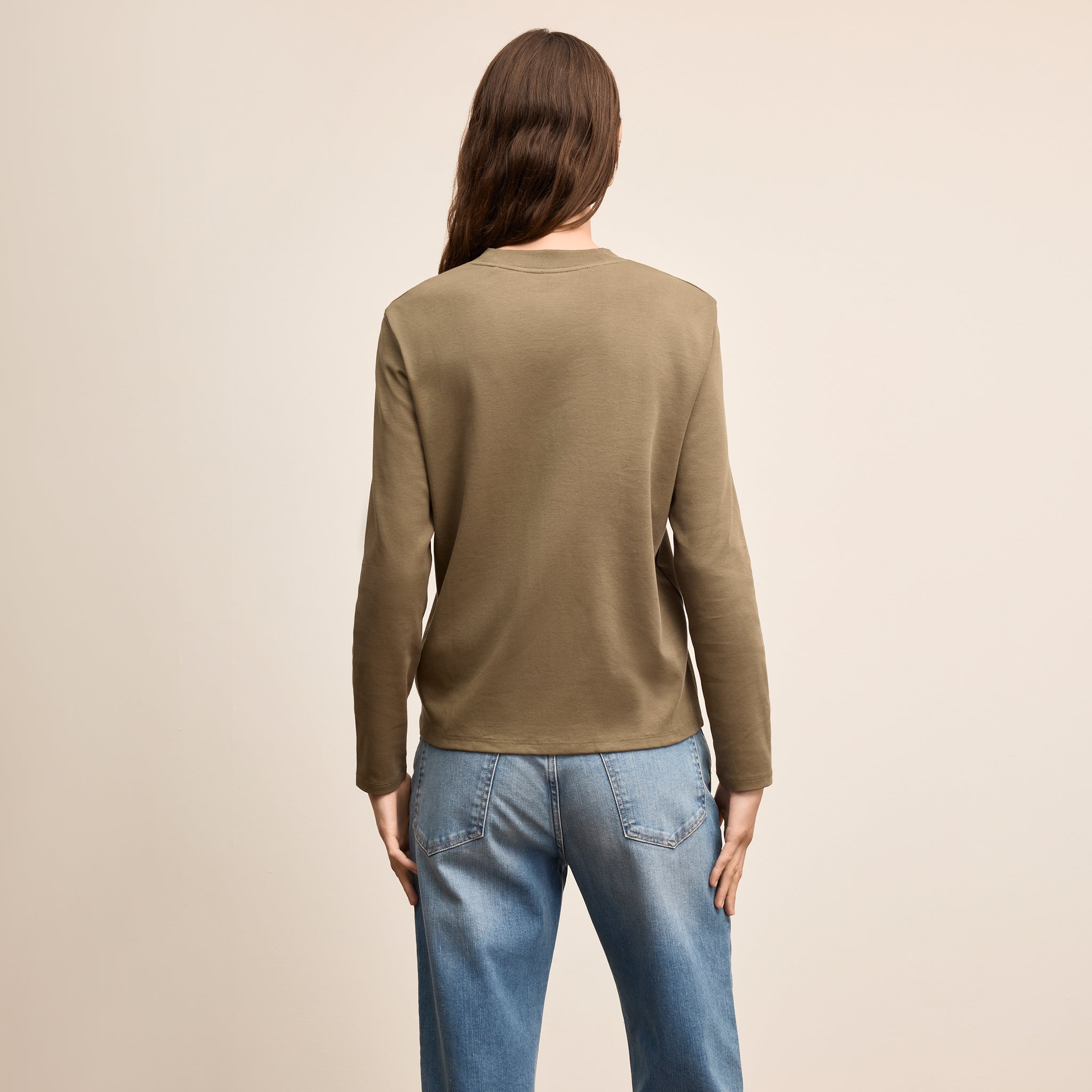 Person wearing a green sweater and blue jeans on a beige background