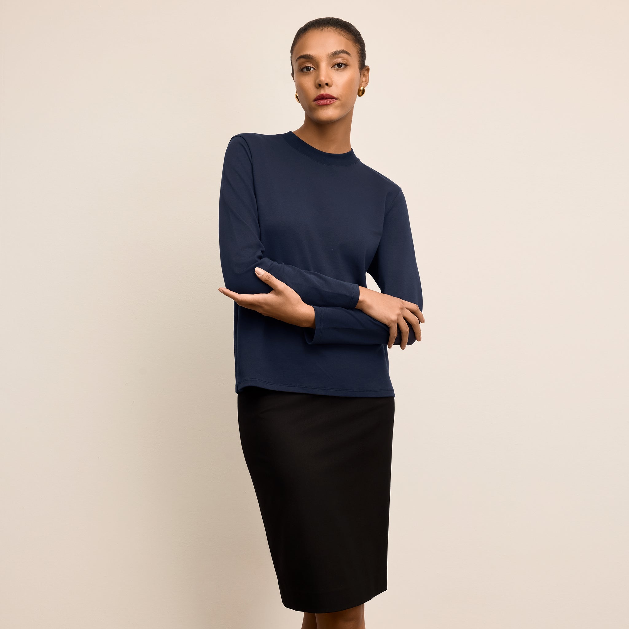 Woman wearing a navy blue sweater and black skirt against a beige background 