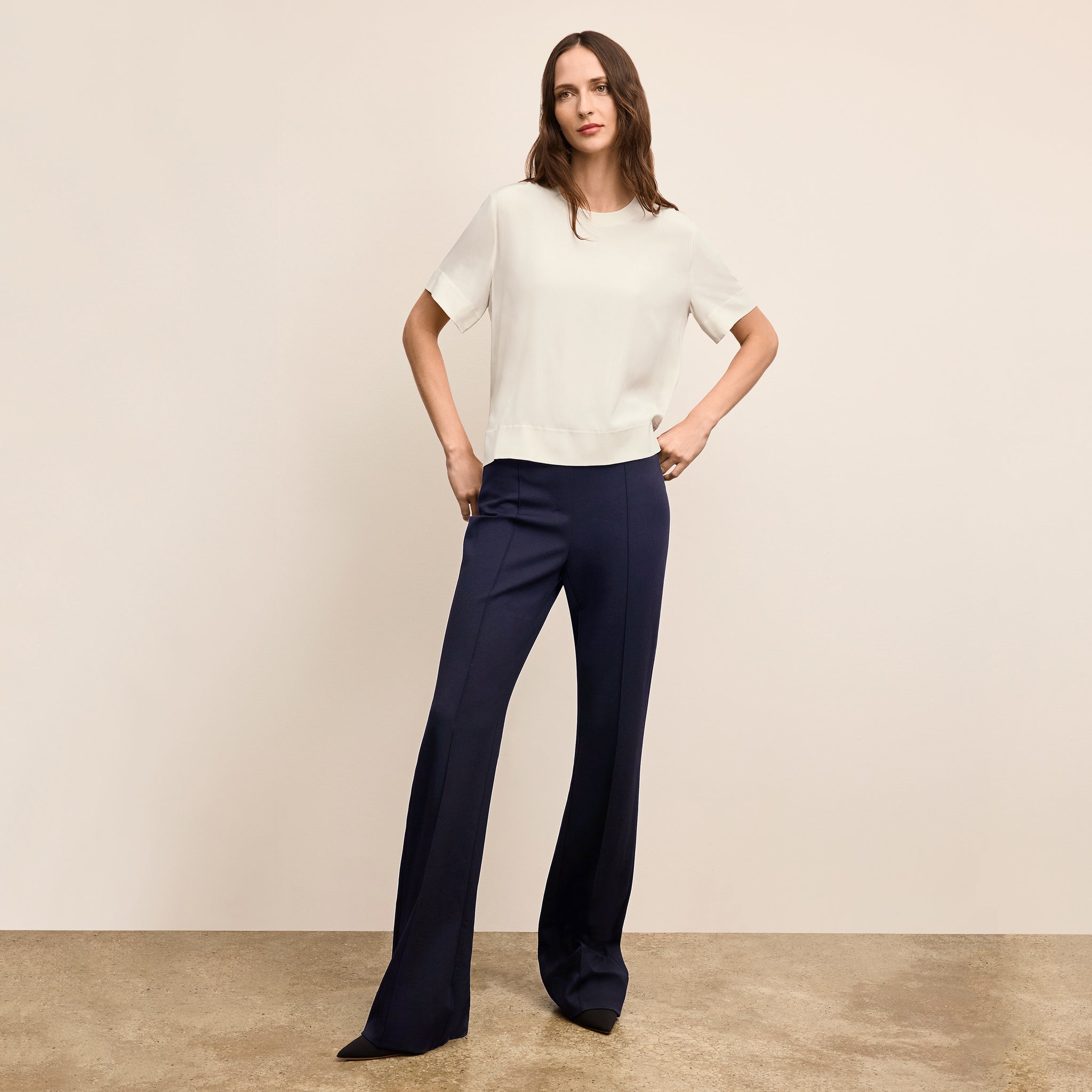 Woman wearing a white top and navy pants against a beige background 