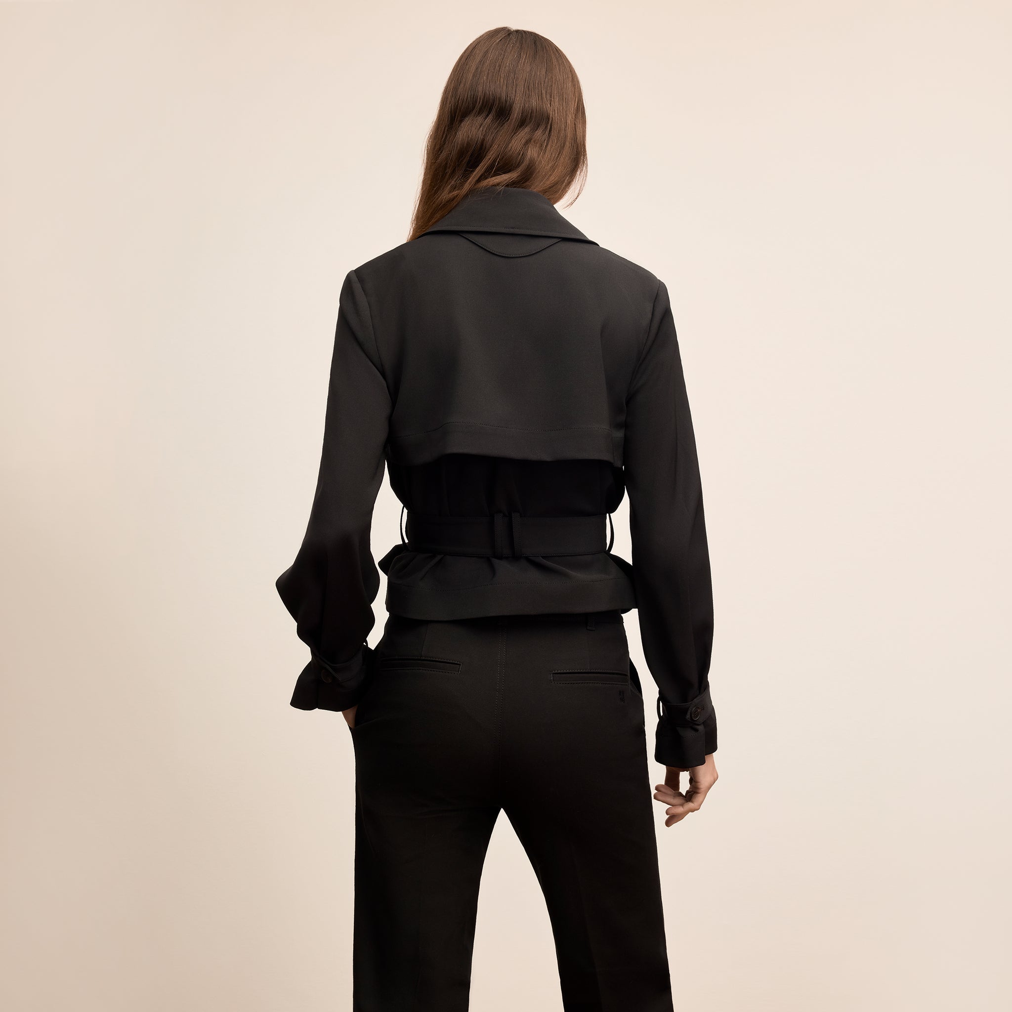 Person wearing a black jacket and pants on a beige background