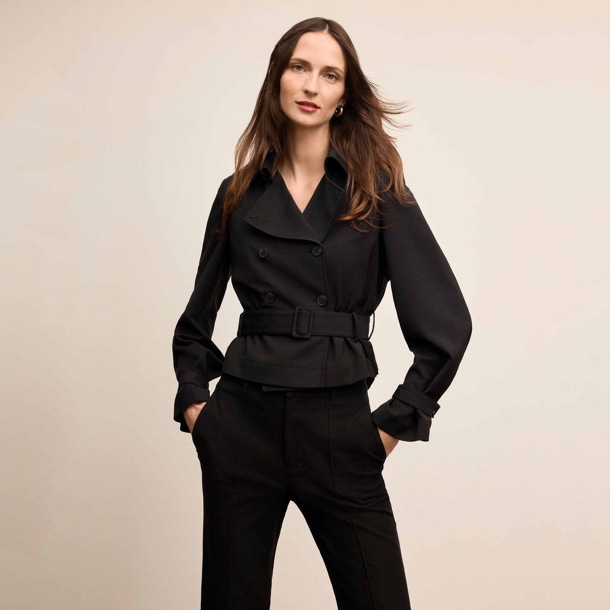 Woman wearing a black coat and pants against a beige background
