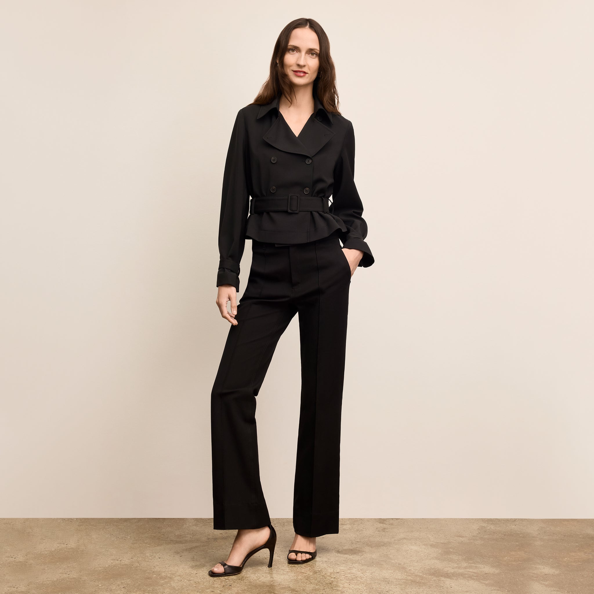Woman wearing a black suit standing against a beige background