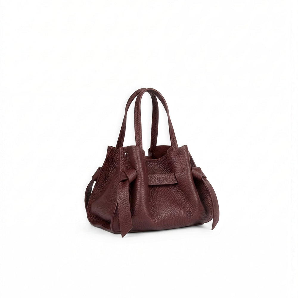 A dark burgundy pebbled leather handbag with double top handles and side ties, shown on a plain white background.