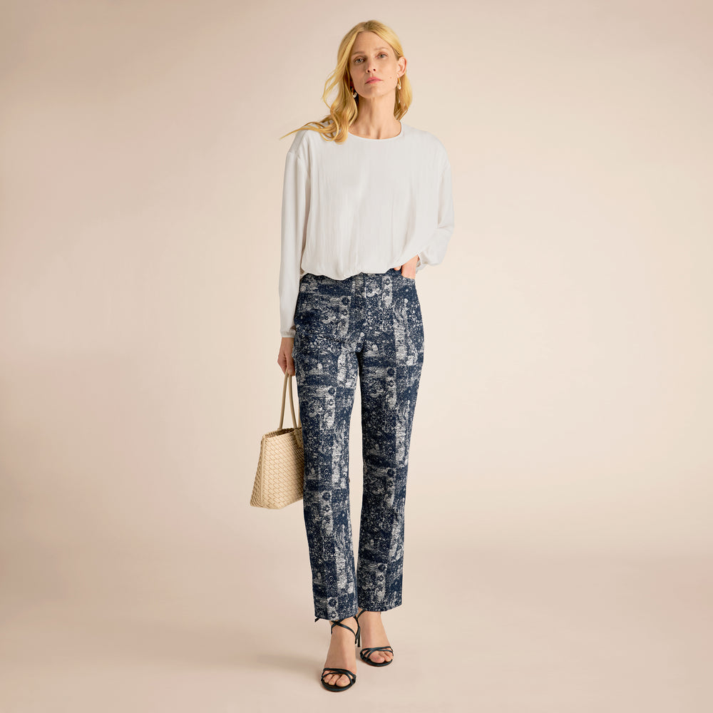 Woman wearing a white top and patterned pants with a beige background