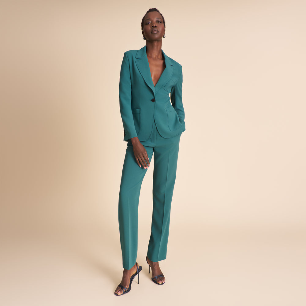 Woman wearing a teal suit against a beige background