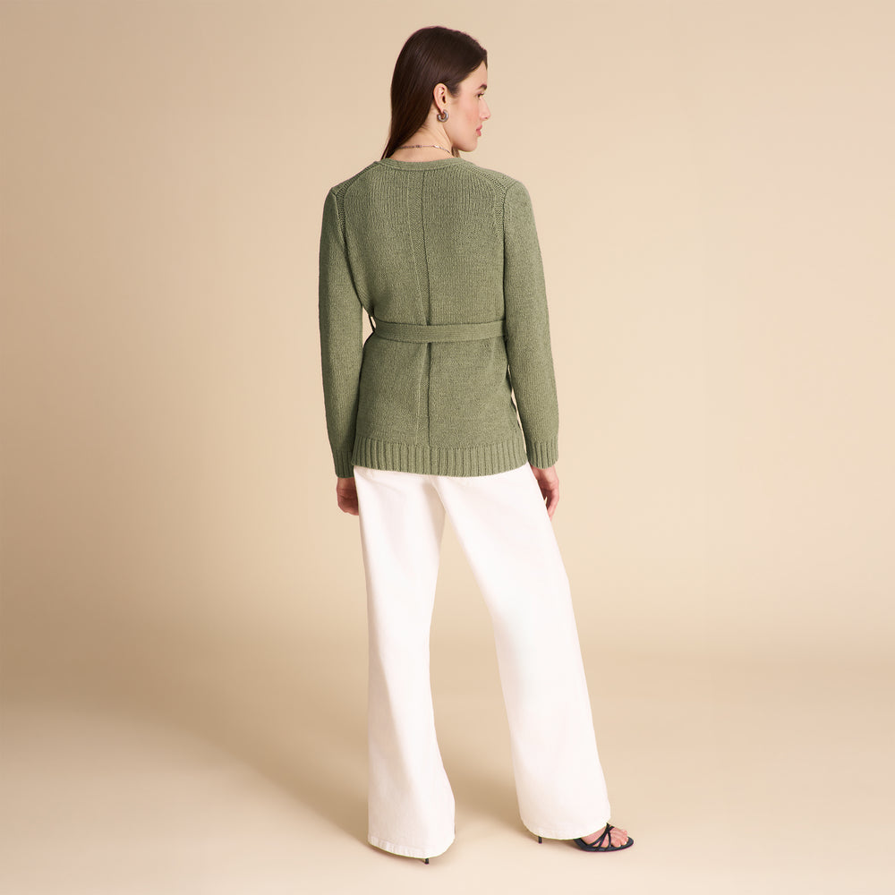 Woman wearing a green sweater and white pants on a beige background