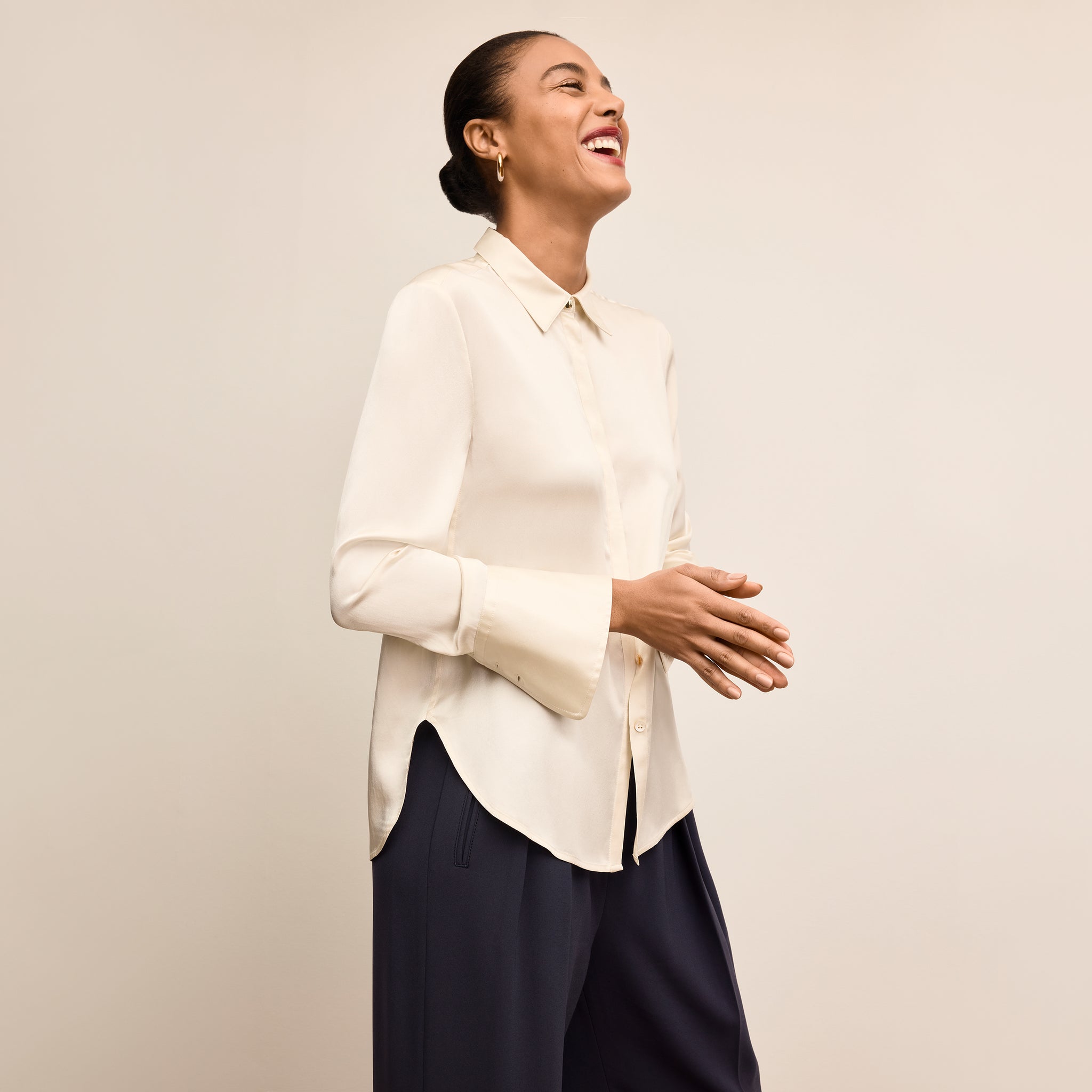 Woman wearing a white blouse and dark pants against a beige background