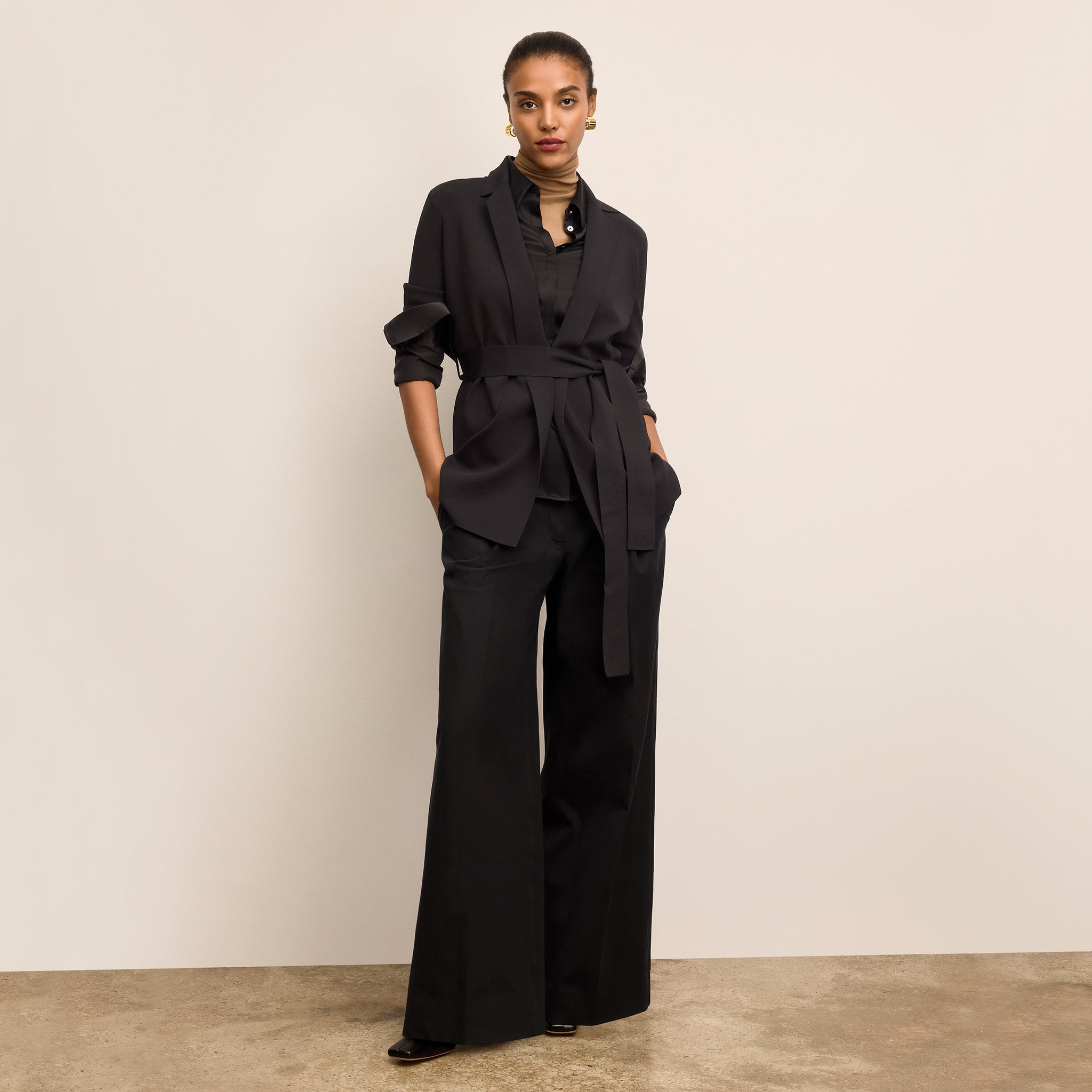 Woman wearing a black outfit with a belt against a beige background